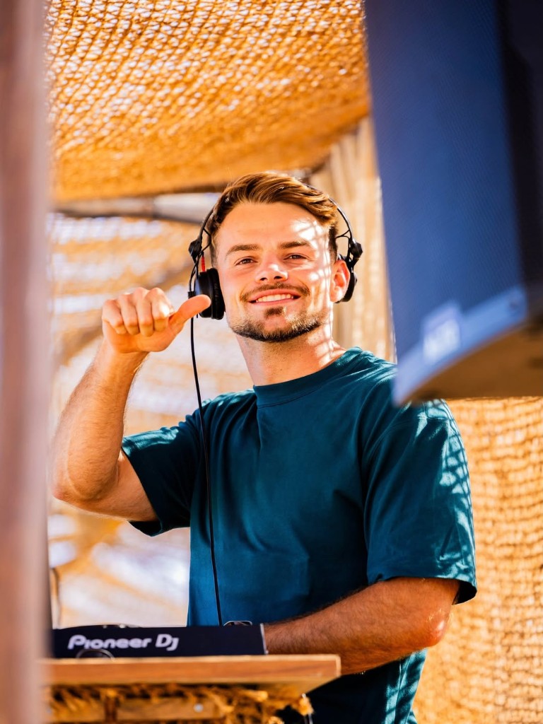 Davon Goodchild behind the decks outdoors, headphones on, giving a thumbs up